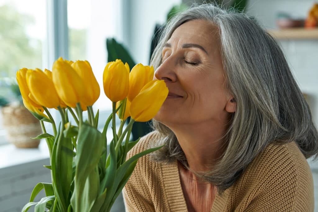 Senior woman smelling yellow tulips, assisted living incentive