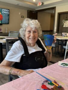 Resident smiling while holding a hand-painted blue cup during a memory care art session.