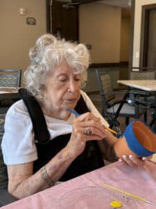 Resident painting a clay pot with blue paint during a memory care art activity.