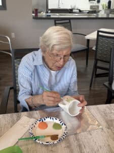 A Meadowview of Davenport memory care resident paints a ceramic mug with colorful designs during a creative activity.