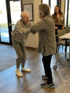 wo Meadowview of Davenport memory care residents smile and hold hands while dancing together indoors, with a team member looking on warmly.
